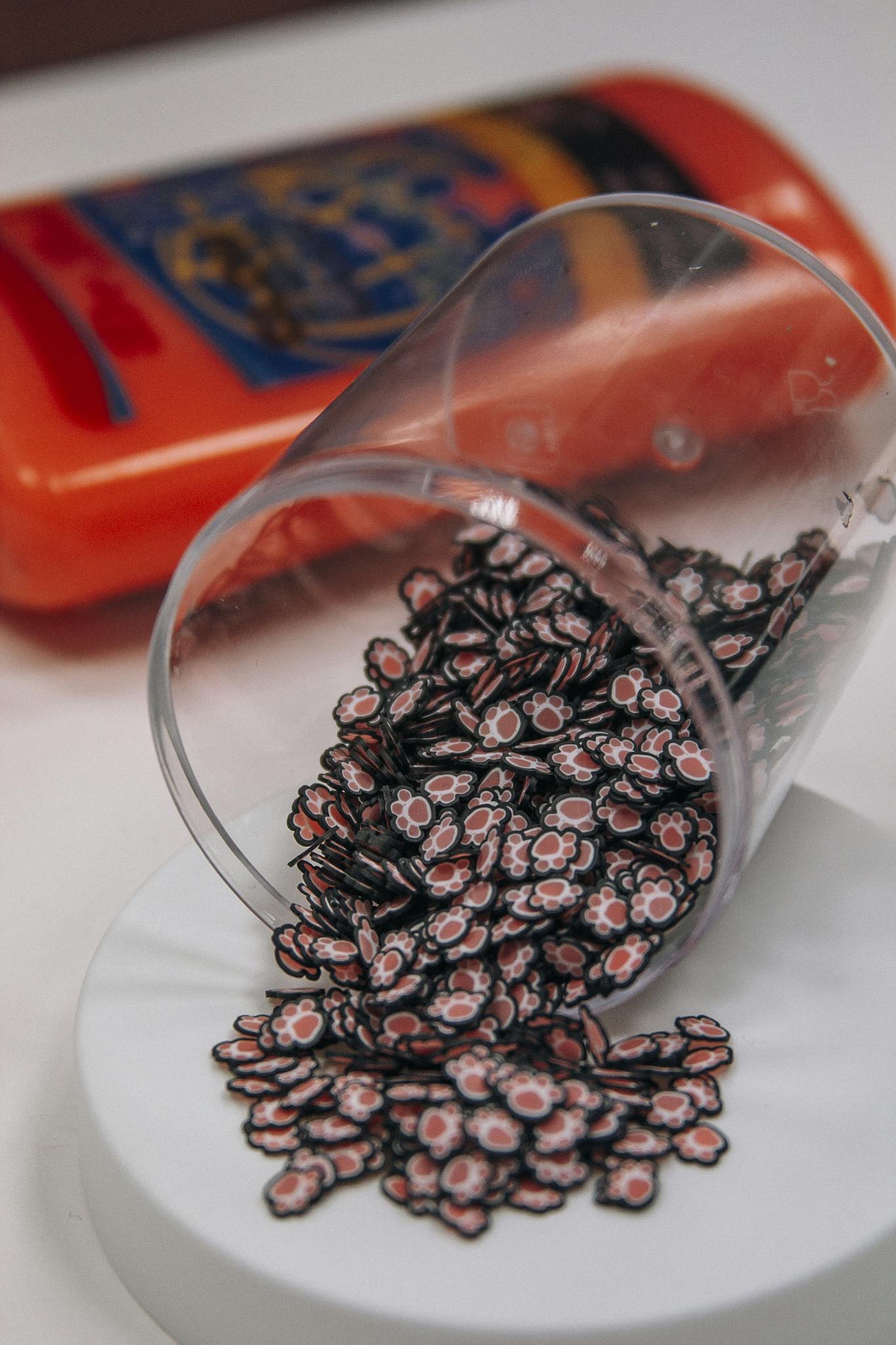 Charming paw-shaped beads spilling from a transparent cup onto a surface.