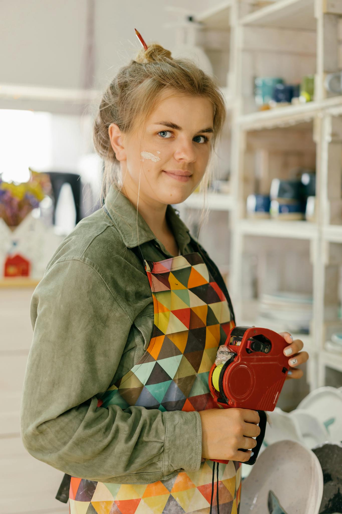 Woman in artistic studio with colorful apron and label maker, embodying creativity.